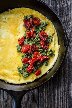 an omelet with tomatoes and spinach in a skillet on a wooden table