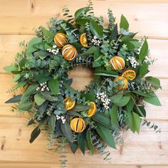 a wreath with oranges and greenery on a wooden surface, ready to be used as an ornament