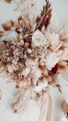 an arrangement of dried flowers, feathers and scissors on a white table with other items