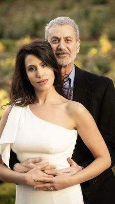 an older man standing next to a woman in a white dress with her hands on her stomach