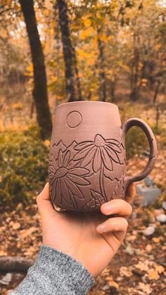 a person holding a coffee mug in their hand while walking through the woods on a fall day