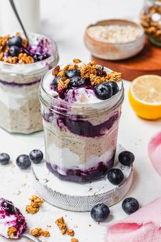 two mason jars filled with blueberry cheesecake and granola toppings on a white table