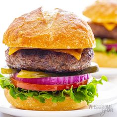 a hamburger with lettuce, tomato and pickles on a white plate next to another burger