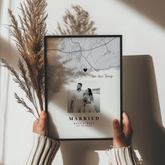 a person holding up a framed photo in front of a plant with the words married on it