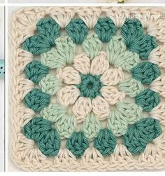 a crocheted square with green and white flowers on it's center, in the shape of a flower