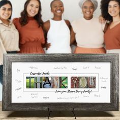 a group of women standing next to each other in front of a wooden frame with writing on it