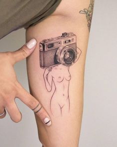 a woman with a camera tattoo on her arm is holding a camera up to the side