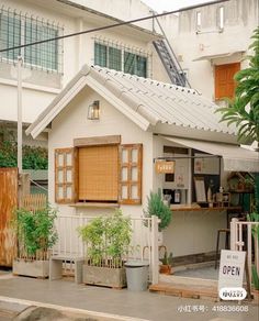 a small white house with an open sign on the front door and plants in pots next to it