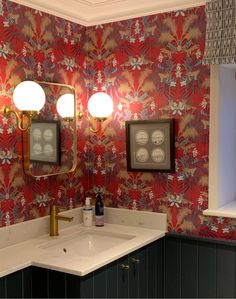 a bathroom with red and green wallpaper, two lights on the vanity and a gold faucet