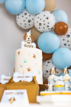 a dog themed birthday party with blue and brown balloons on the wall, cake and cupcakes