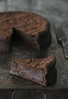 a chocolate cake with one slice missing from it on a metal tray next to a knife