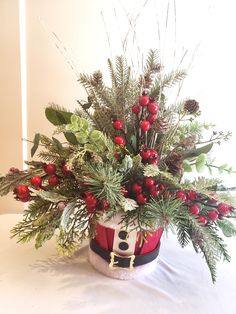 a christmas centerpiece with holly, berries and pine cones in a red basket on a white table cloth