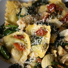 a white bowl filled with pasta and spinach covered in cheese on top of a wooden table