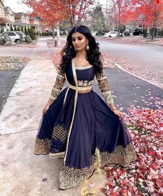 a woman in a blue and gold dress standing on the sidewalk with leaves all around her