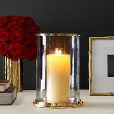 a lit candle sitting on top of a table next to two framed pictures and red roses