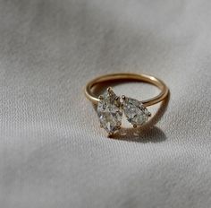 an engagement ring with two pear shaped diamonds on the side, sitting on a white cloth