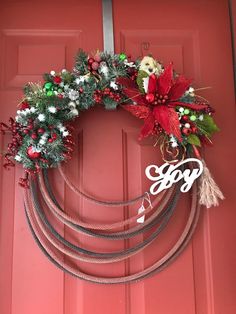 a christmas wreath on a red door with the word joy hanging from it's side