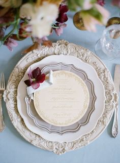 the table is set with white plates and silverware, purple flowers, and napkins