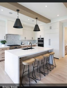 a kitchen with three stools next to an island and two lights hanging from the ceiling