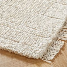 a white rug with fringes on top of a wooden floor next to a wood floor