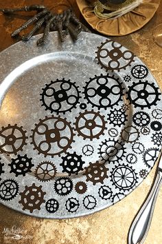 a metal plate with gears on it sitting on a table next to silver utensils