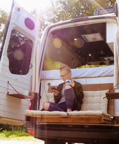 an older woman sitting on the back of a truck looking at her cell phone while holding a camera