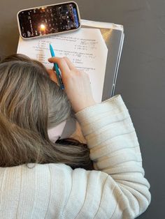 a woman writing on a piece of paper with a cell phone above her head