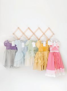 four dresses hanging on a clothes rack against a white wall, one is pink, the other is yellow