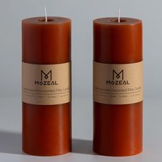 two candles with labels on them sitting next to each other in front of a gray background