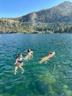 three people swimming in the water with mountains in the background