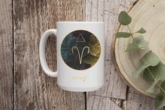 a white coffee mug sitting on top of a wooden table next to a green plant