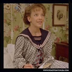 a woman sitting on top of a bed next to a wallpapered room with flowers