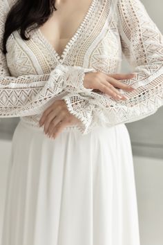 a woman wearing a white dress with long sleeves and lace on her arms, posing for the camera