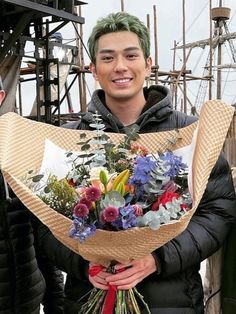 a man with green hair holding a bouquet of flowers in front of another man wearing a black jacket