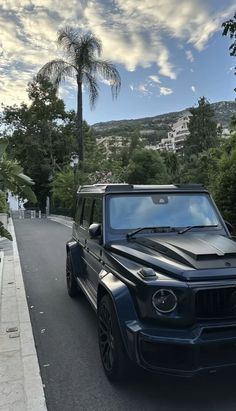 a black mercedes g - class parked on the side of a road with palm trees in the background