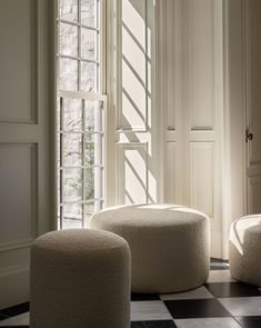 two white stools sitting on top of a black and white checkered floor