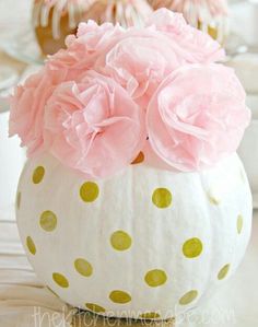 a polka dot pumpkin with pink flowers in it sitting on top of a wooden table