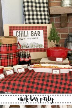 a red and black plaid table cloth with chili bar sign on it next to other food items