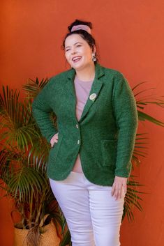 a woman standing next to a potted plant wearing a green jacket and white pants