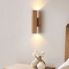 a white vase sitting on top of a wooden table next to a wall mounted light