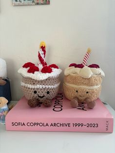 two crocheted cupcakes sitting on top of a pink book next to a teddy bear