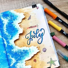 an open notebook with the words hello july written on it next to markers and pencils