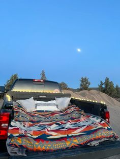 a bed in the back of a pickup truck with a blanket on it's flatbed