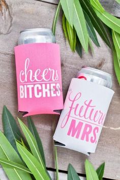 two pink and white can coolers sitting on top of a wooden table next to green leaves