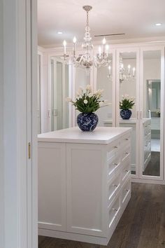 a white kitchen with chandelier and blue vases on the center island in front of it