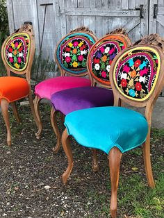 four colorful chairs sitting next to each other in front of a wooden fence with flowers painted on them