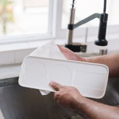 a person holding a white tray over a kitchen sink