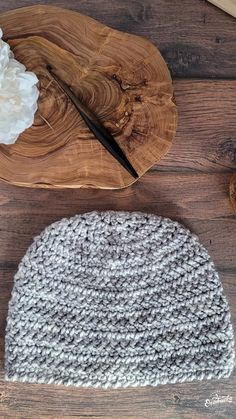 a knitted hat sitting on top of a wooden cutting board next to a flower