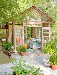 a garden shed with lots of potted plants and flowers in the foreground, surrounded by greenery