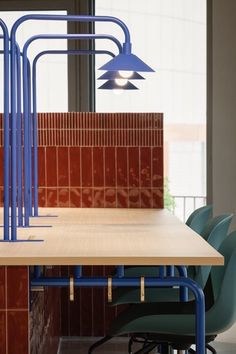 a wooden table with blue chairs in front of a tiled wall and window behind it